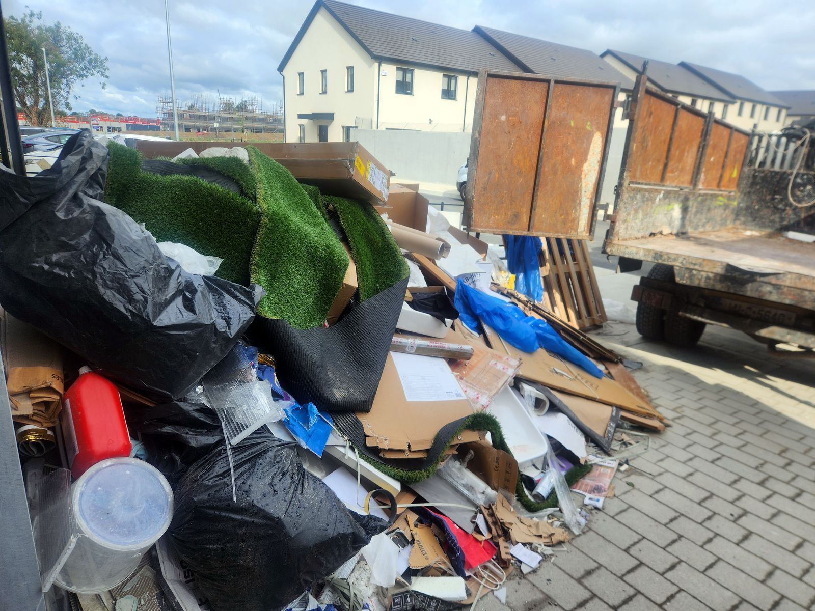 Large pile of rubbish bags, artificial grass, cardboard and pallets on paving