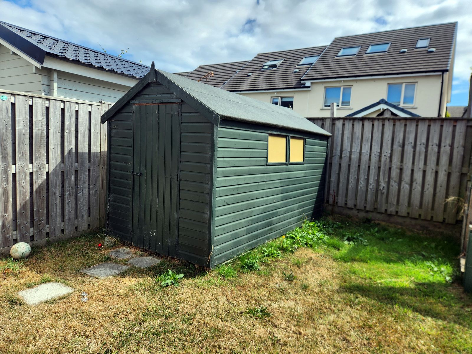 Green wooden shed in a back garden before removal
